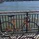 A photo of a bright orange bike leaning against a railing.